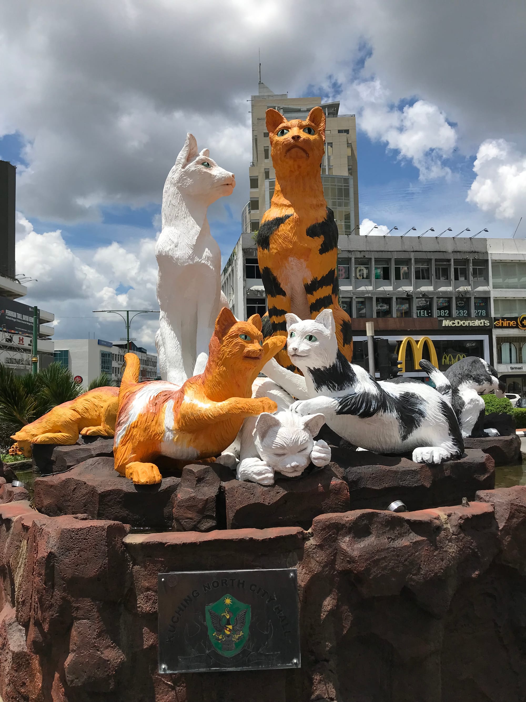 A sculpture of 8 cats. 2 are sitting; 3 kittens are playing in front of the seated cats. 2 more kittens are on the side. 