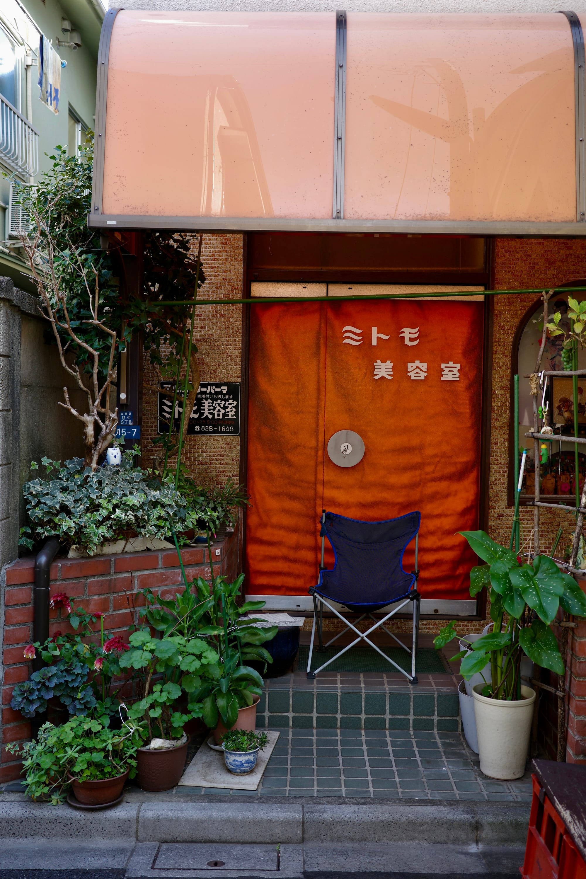 A blue camping chair sits in front of an orange door, surrounded by potted plants.