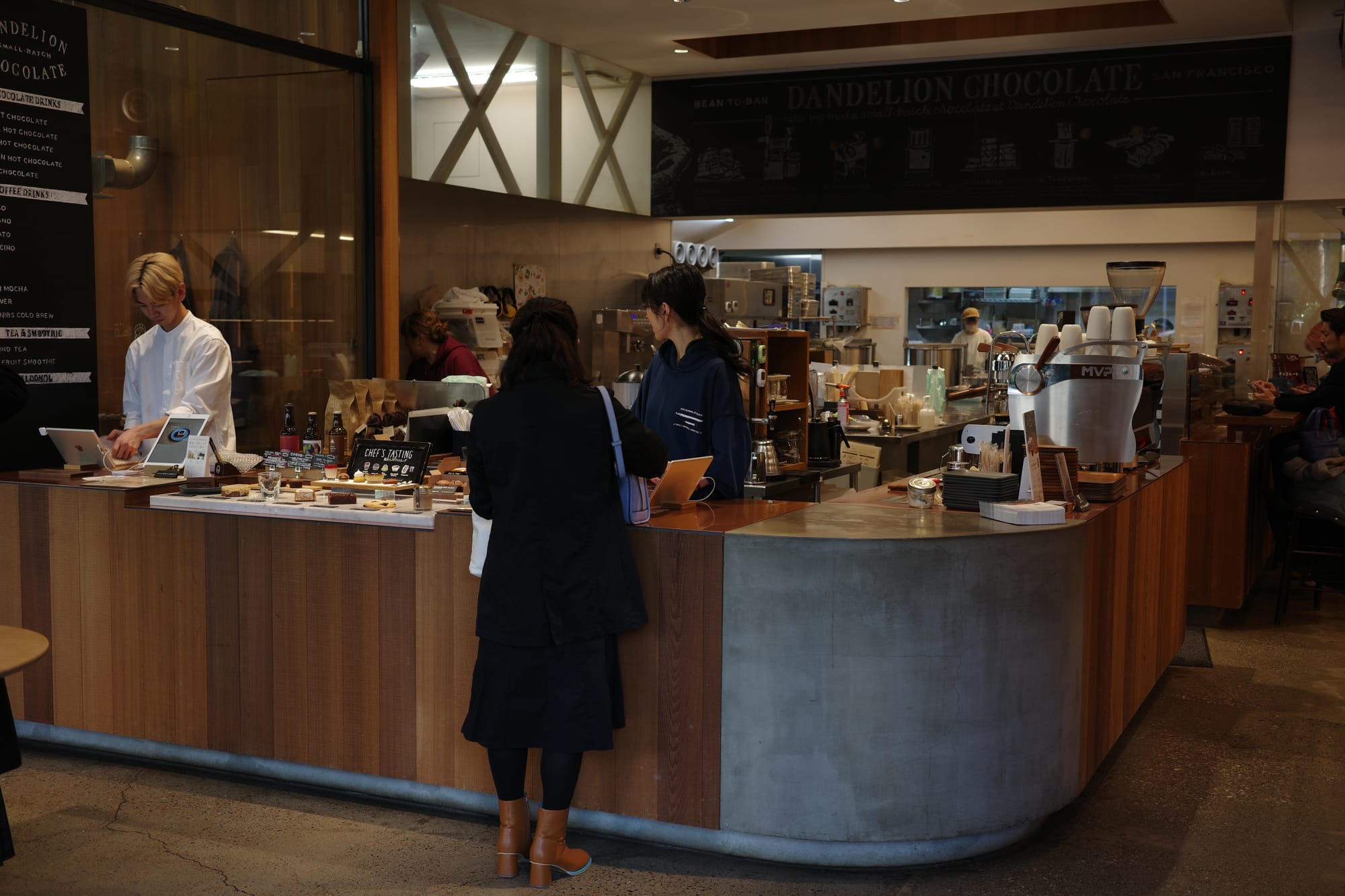 Interior shot of Dandelion cafe. There is a long curved counter. A man is at the cashier and a lady is picking up her order from a female staff member.