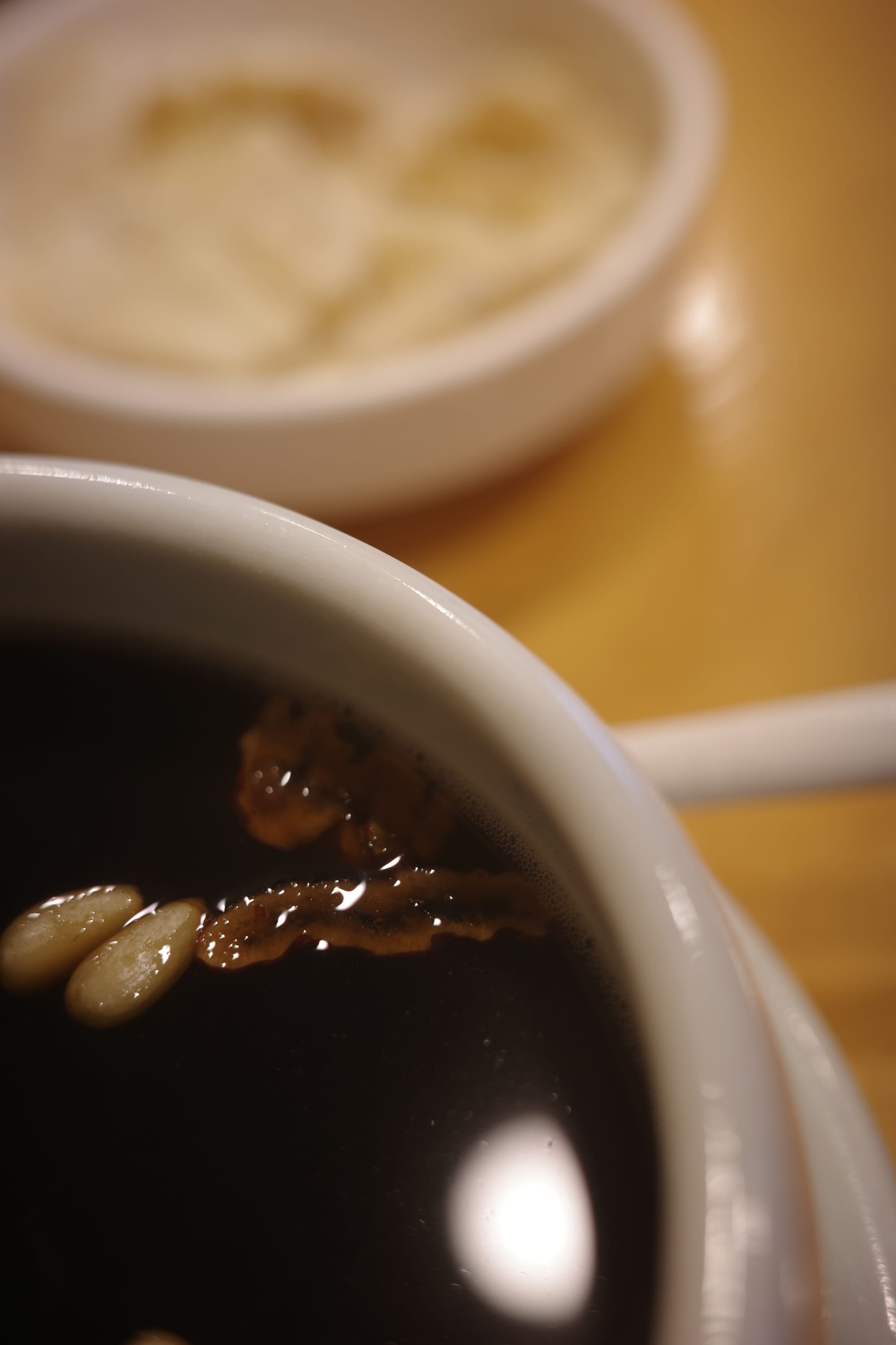 Close up shot of a bowl of black herbal tea with some pine nuts and red date pieces floating on the surface.