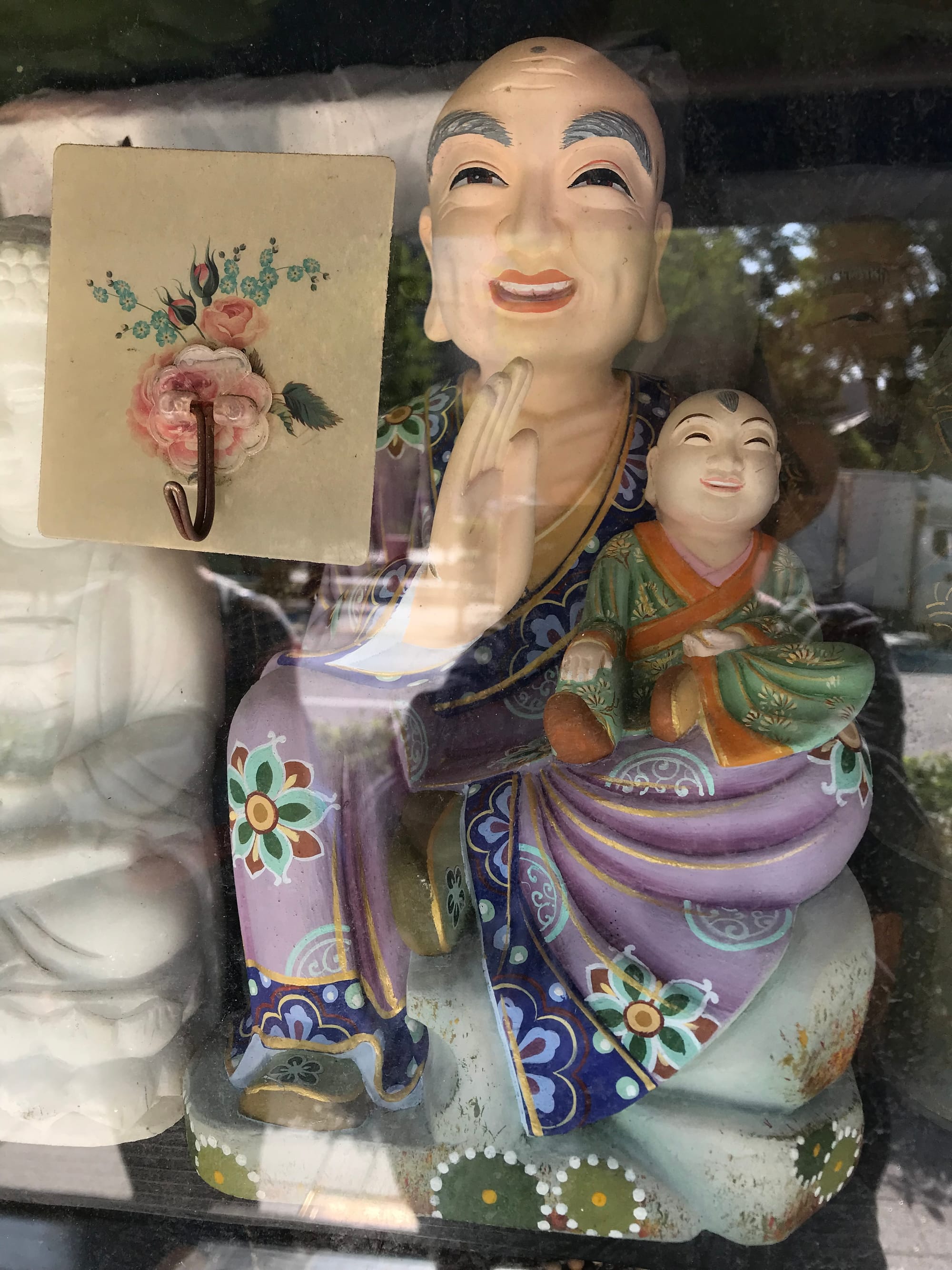 A colourful porcelain Buddha holding a young boy sits in a glass-fronted case.