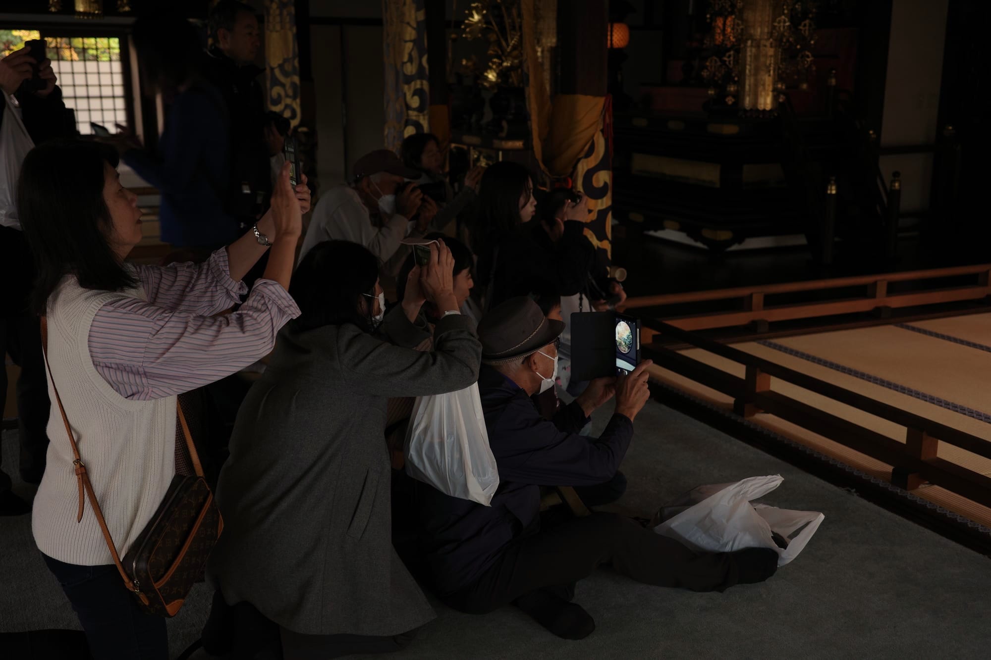 A crowd (three people deep) are taking photos inside a temple