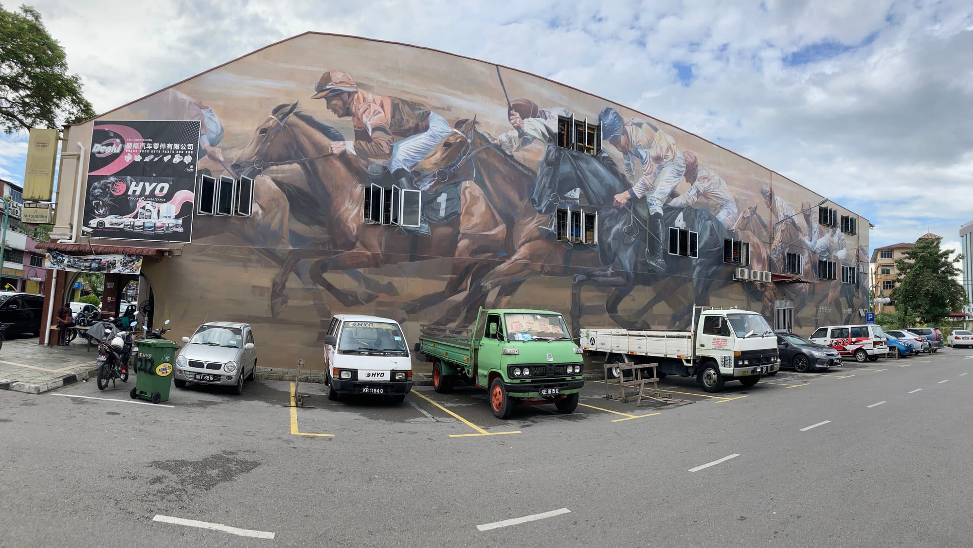 A wide shot of a mural of race horses with vehicles parked in front of it