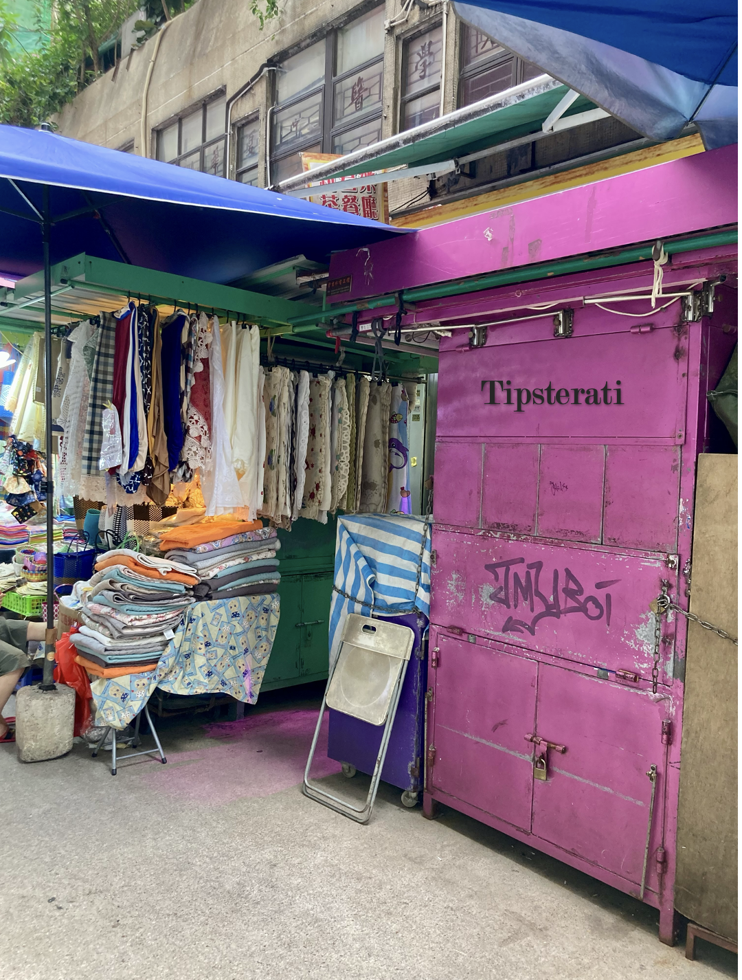 A shuttered street stall (in purple) stands next to another selling towels and blankets.