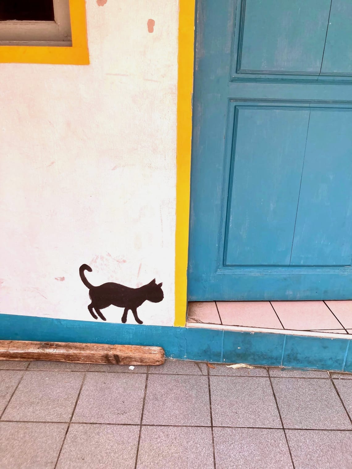 A mural of a small, black cat painted next to a blue door.