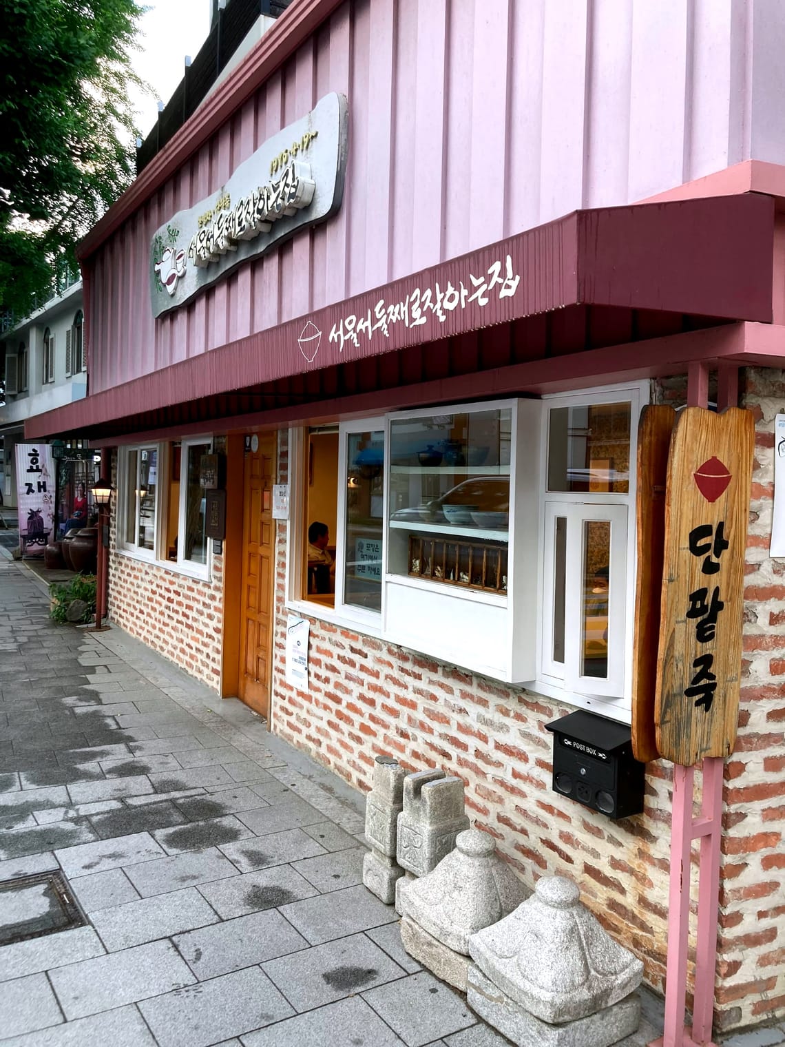 A red-brick building with white windows and a burgundy awning and mauve facings above it. 