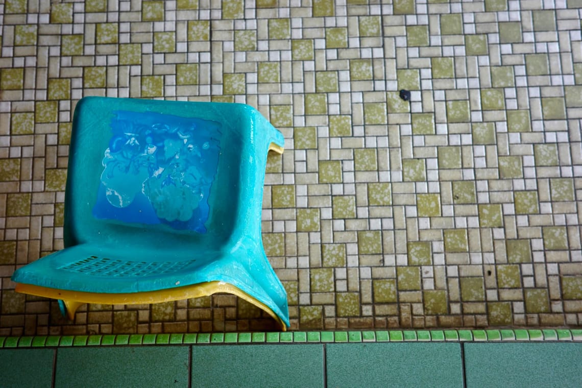 Mosaic floor tiles in shades of chartreuse and white. There are two plastic stacked chairs in the bottom left. 