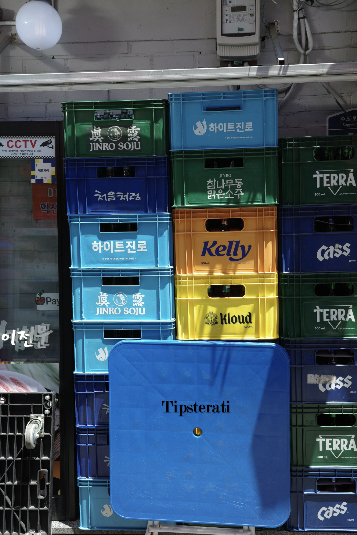 A blue foldable table stands in front of stacks of colourful beer and soju crates.