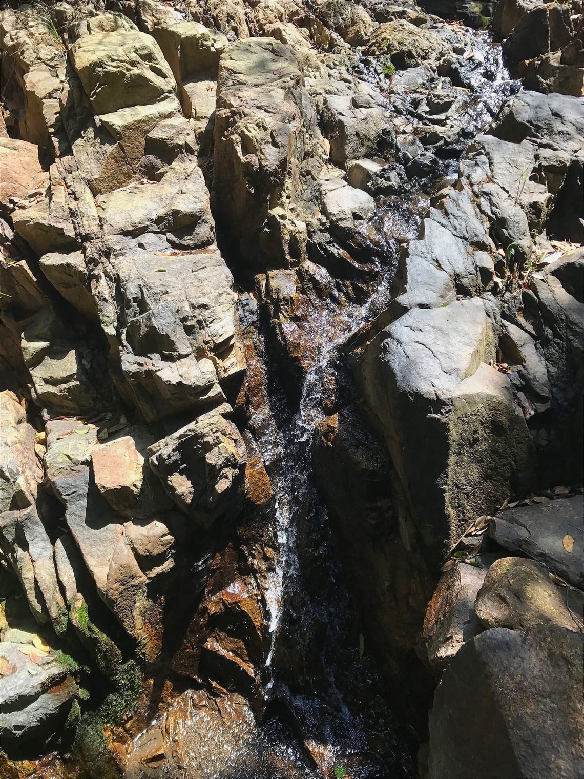 A small channel of water gushes through some angular rocks.