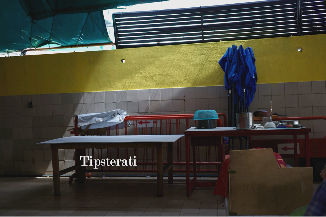 Sunlight streams down onto two tables and some stored railings by a wall.