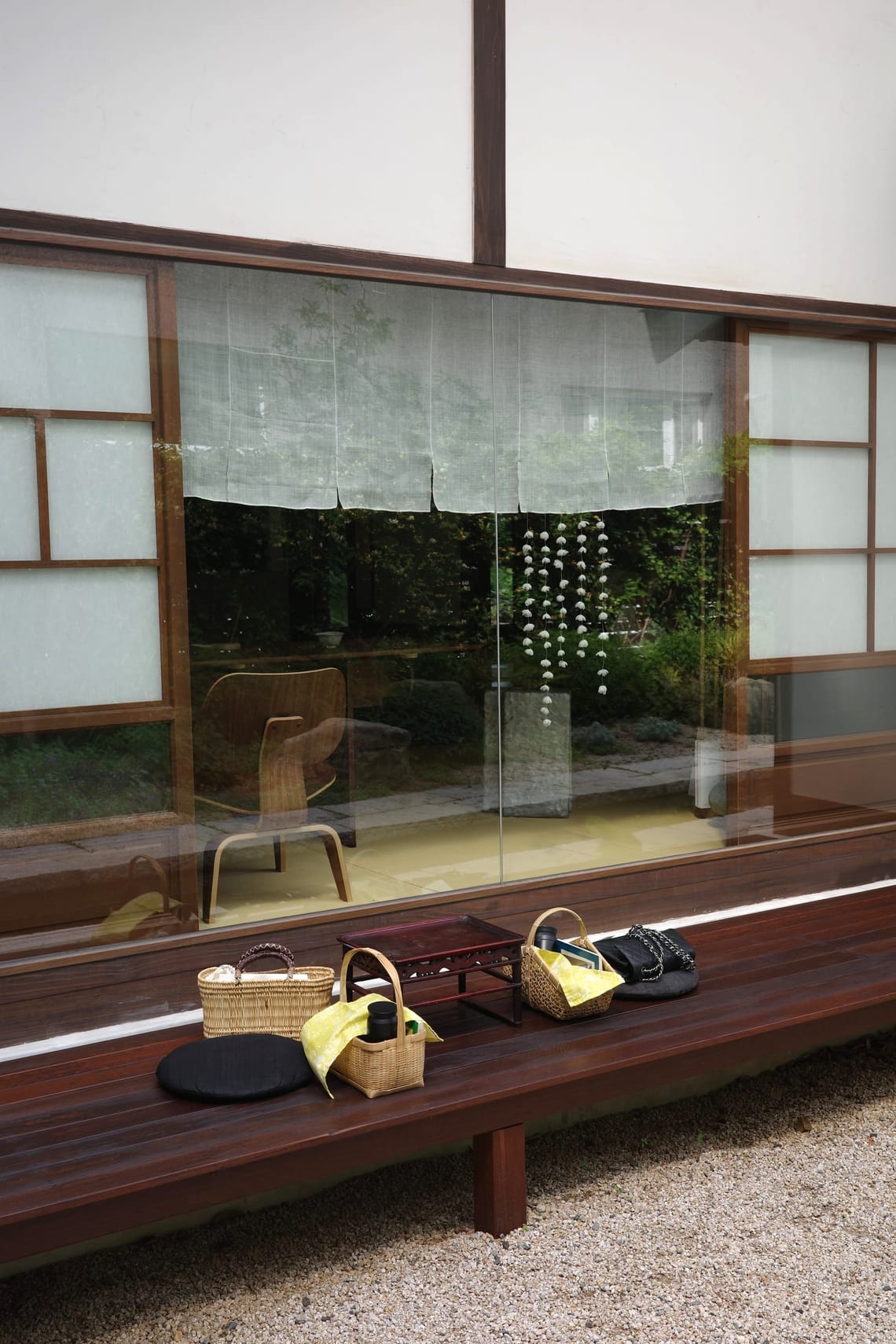 Two picnic baskets and ladies' handbags are on a wooden platform in front of window of a Japanese house.