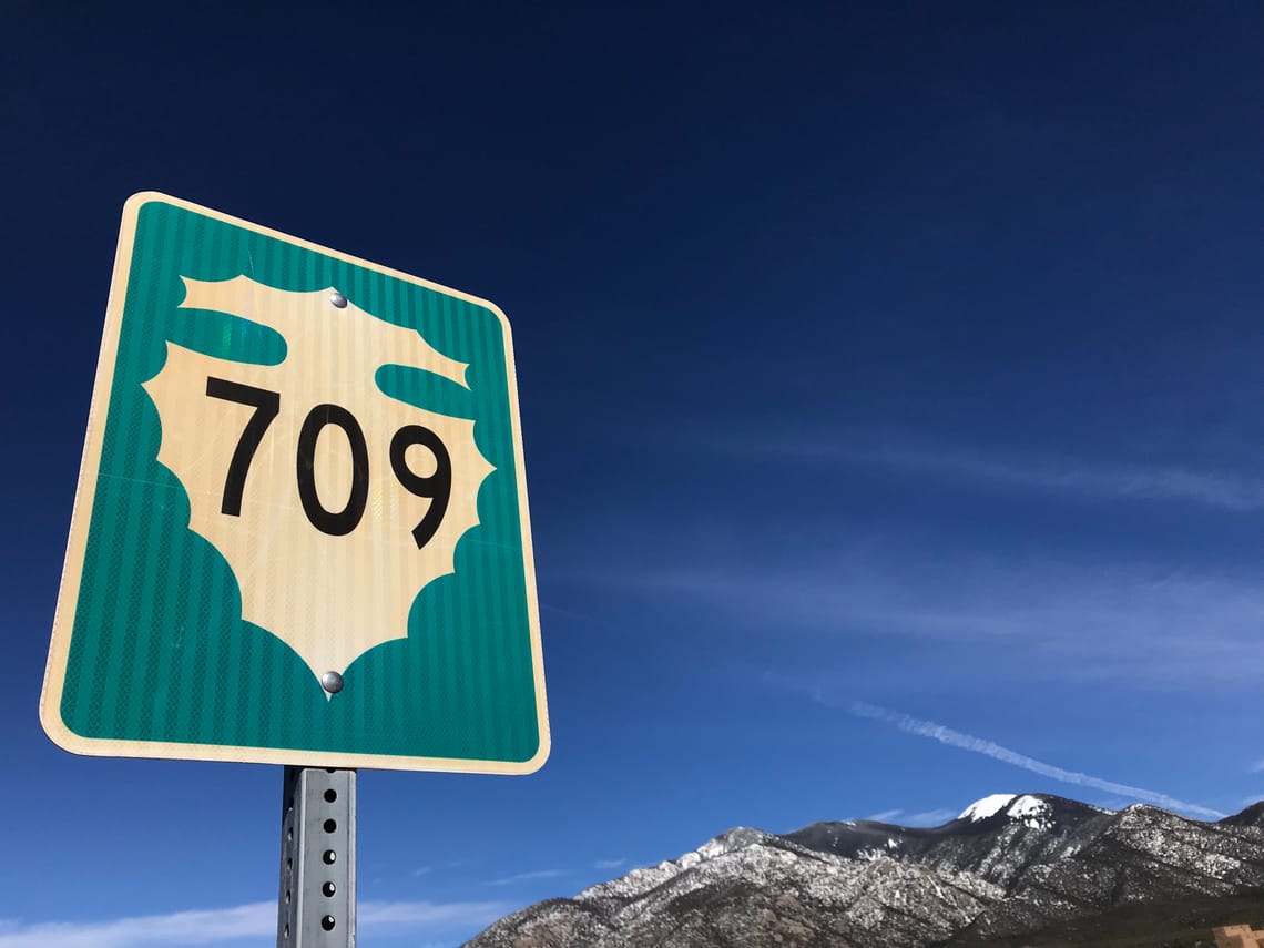 A Route 709 sign in the foreground and the Taos Mountains are in the background.