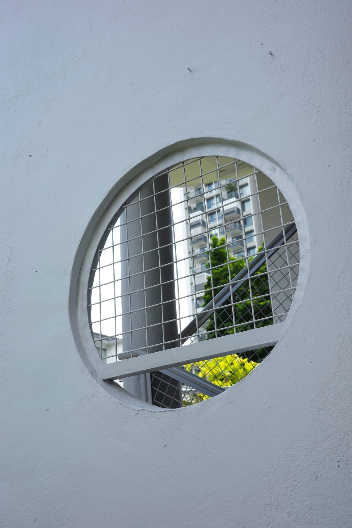 A round window on a wall reveals a glimpse of trees and a skyscraper in the distance